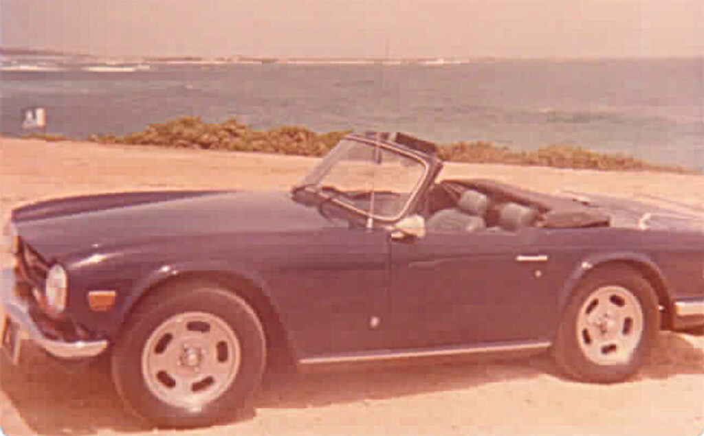 A black car parked on the beach near water.