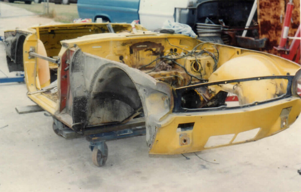 A yellow car that is broken down and sitting in the sand.