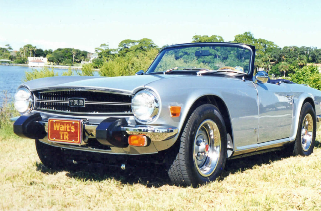 A silver car parked in the grass near some trees.