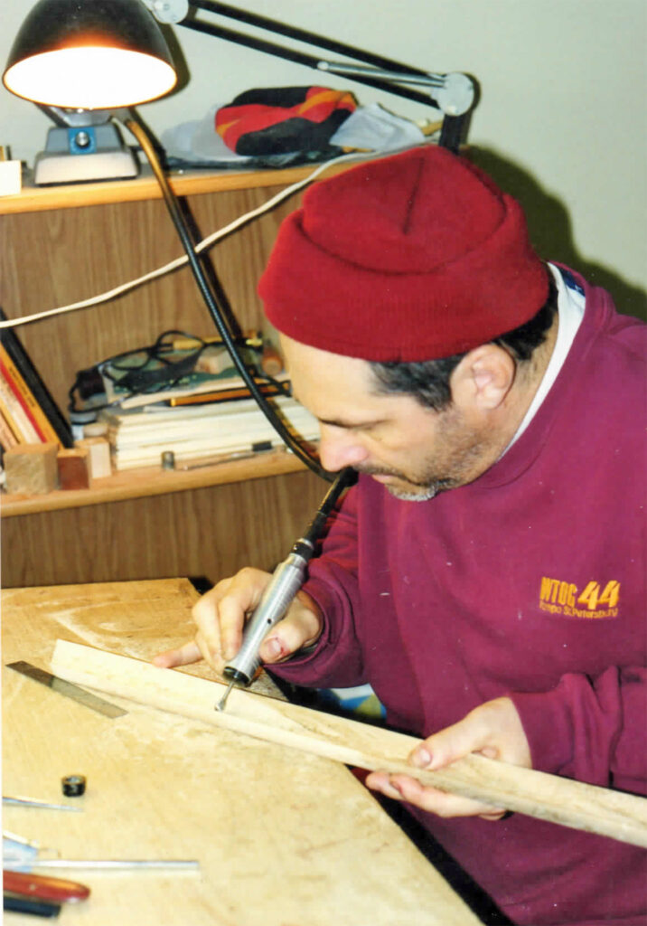 A man in red shirt writing on wooden board.